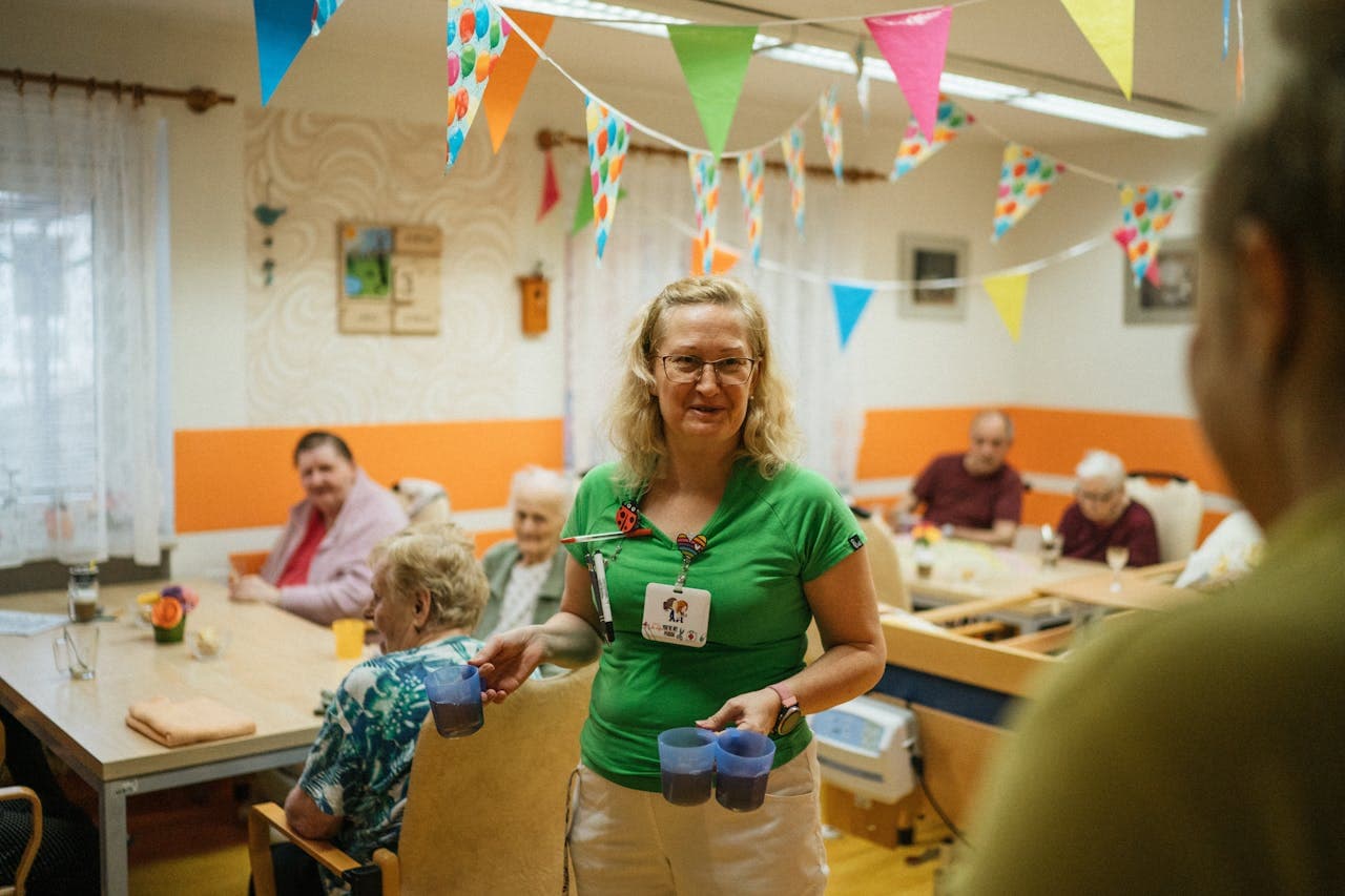 A care worker bringing drinks to residents in a bright common room.